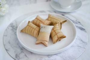 Lepet or Leupeut is a type of snack made from glutinous rice mixed with peanuts, cooked in coconut milk, then wrapped in coconut leaves. Close up view photo