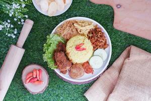 indonesian style yellow rice with minced chicken in white plate on green grass background photo