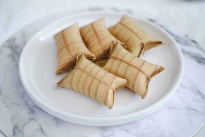 Lepet or Leupeut is a type of snack made from glutinous rice mixed with peanuts, cooked in coconut milk, then wrapped in coconut leaves. Close up view photo
