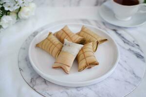 Lepet or Leupeut is a type of snack made from glutinous rice mixed with peanuts, cooked in coconut milk, then wrapped in coconut leaves. Close up view photo