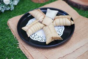 Lepet or Leupeut is a type of snack made from glutinous rice mixed with peanuts, cooked in coconut milk, then wrapped in coconut leaves. Close up view photo