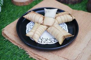 Lepet or Leupeut is a type of snack made from glutinous rice mixed with peanuts, cooked in coconut milk, then wrapped in coconut leaves. Close up view photo