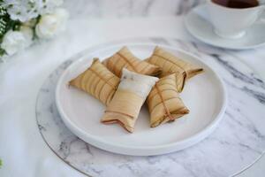 Lepet or Leupeut is a type of snack made from glutinous rice mixed with peanuts, cooked in coconut milk, then wrapped in coconut leaves. Close up view photo