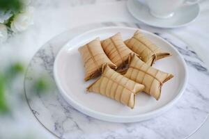 Lepet or Leupeut is a type of snack made from glutinous rice mixed with peanuts, cooked in coconut milk, then wrapped in coconut leaves. Close up view photo