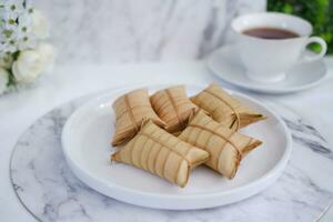 Lepet or Leupeut is a type of snack made from glutinous rice mixed with peanuts, cooked in coconut milk, then wrapped in coconut leaves. Close up view photo