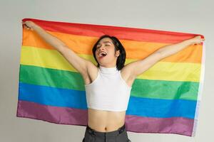 Image of Asian gay man holding a rainbow flag confidently posing on a white background photo