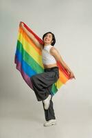 Image of Asian gay man holding a rainbow flag confidently posing on a white background photo