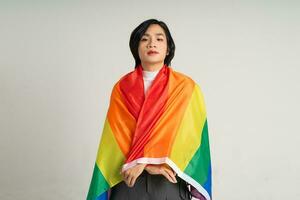 Image of Asian gay man holding a rainbow flag confidently posing on a white background photo