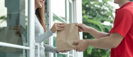 Happy smiling Asian woman receives paper bag parcel of food from courier front house. Delivery man send deliver express. online shopping, paper container, takeaway, postman, delivery service, packages photo