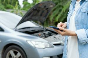 breakdown, broken car, repair. Woman uses mobile phone check insurance premiums through application due to car accident . Find garage to get car fixed during country tour, waiting for help, emergency. photo