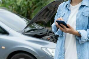 breakdown, broken car, repair. Woman uses mobile phone check insurance premiums through application due to car accident . Find garage to get car fixed during country tour, waiting for help, emergency. photo