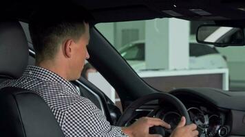 hermoso hombre sonriente terminado su hombro demostración pulgares arriba, sentado en un nuevo coche video