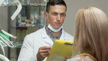 Young male dentist talking to his female patient, examining medical papers video
