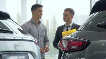 Selective focus on a car, male customer talking to auto dealer on the background video