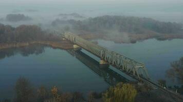 aéreo Visão do a estrada de ferro ponte sobre a rio dentro a névoa dentro a cedo manhã video