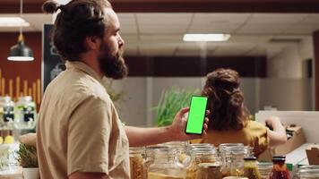 Man using green screen smartphone in zero waste supermarket to check ingredients for healthy recipe. Client in local grocery shop uses chroma key phone while shopping for organic veggies video