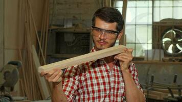 Bearded carpenter examining wood piece after grinding it video