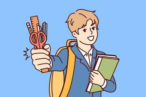 Little boy from primary school with smile demonstrates stationery and books, standing with backpack photo