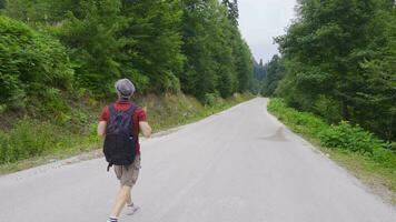 Man in hat with backpack walking on empty road. video