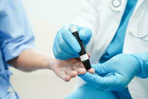 Asian doctor using lancet pen on senior patient finger for check sample blood sugar level to treatment diabetes. photo