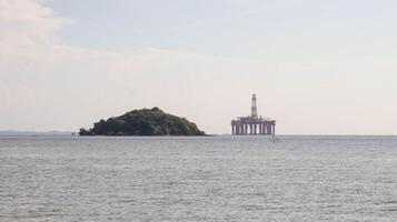 Offshore oil platform drilling site or oil rig project seen far in the middle of the sea and an island. photo