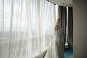 hermosa blanco Boda vestir en un blanco maniquí en el habitación con grande ventana foto