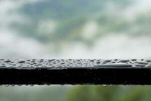 Raindrops cling to the iron balcony railing. Mountain view background and water vapor in the rainy season. Soft and selective focus. photo