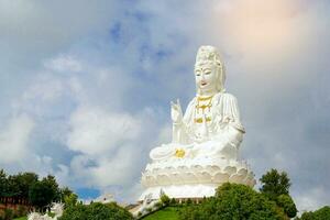 A large white Kuan Yin statue is erected on top of a mountain. It is a god according to Mahayana beliefs. and is believed to be a bodhisattva who has compassion for all human beings. photo