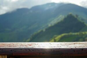 A long wooden bench without a backrest act as a balcony to sit and relax, admiring the mountain view and the rainy season mist, white streaks covering the mountains like fluffy clouds. photo