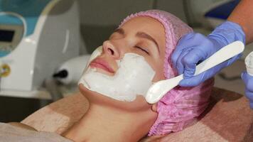 Happy woman smiling during facial mask application at beauty salon video