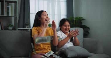 Footage of a young woman and teenage girl enjoying scattering cash bills on a sofa in the living room at home. video