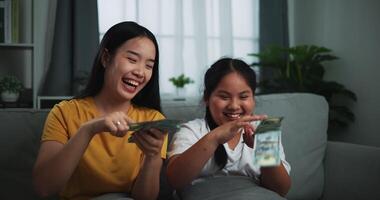 Footage of a young woman and teenage girl enjoying scattering cash bills on a sofa in the living room at home. video