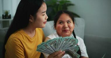 metraggio di giovane asiatico donna mostrando dollaro a telecamera e sorridente su divano nel il vivente camera a casa. video