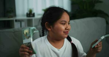 imágenes de alegre adolescente niña demostración dólar a cámara y sonriente en sofá en el vivo habitación a hogar. video