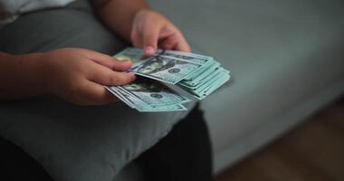 Footage close up hands of young Asian woman enjoy counting cash dollars banknotes on sofa in the living room at home. video