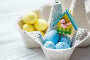 A bunch of yellow and blue eggs in egg carton. near the house with a bird. The concept of an abandoned home of Ukraine for the Easter holiday. photo