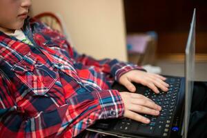 boy in plaid shirt does lessons on laptop. child learns remotely during quarantine of coronavirus. Online learning from home. photo