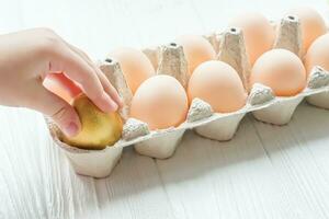The child takes out a golden egg from the egg tray. A dozen chicken eggs on the table. Rise in price of products in Ukraine. New egg prices photo