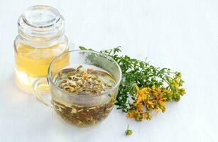 Transparent cup of St. John's wort remedy beverage with bunch fresh Hypericum yellow flowers. jar of spring honey. Medicinal herbs for Alternative Medicine and Homeopathic Remedies photo