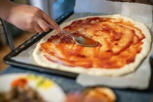 chef makes pizza heart for Valentine's Day holiday. child smears pizza with tomato sauce at home on table. Lifestyle concept. Home-cooked food on self-isolation during coronavirus photo