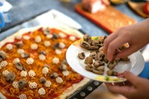 Hand adding mushrooms to the pizza. chef makes pizza heart for Valentine's Day holiday at home on table. Lifestyle concept. Home-cooked food on self-isolation during coronavirus photo