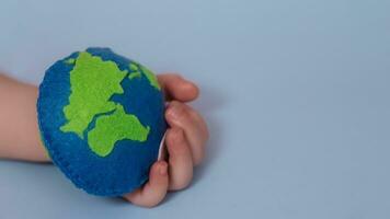 small child holds Earth. palm of child with thimble of felt in form of planet. Saving Ecology with children. Cosept Earth Day.World ocean day, saving water campaign photo