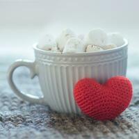 A big crochet red heart next to a cup of cocoa. Cappuccino in a gray cup against a white background. photo