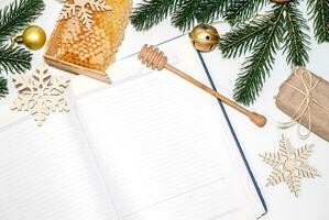 Cellular honey in wooden frame near empty notebook for records. Christmas background with branches of New Year's spruce, golden balls and snowflakes, face mask photo