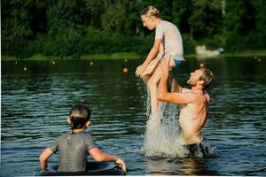 father plays with children in summer in river. Dad throws teenager's son over water. Family Concept photo