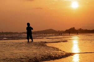 Silhouette of boy walking on the beach at sunset photo