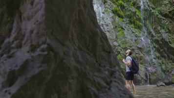 Barefoot teenager looking around in front of waterfall. video