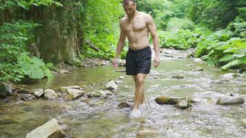 A man in slippers walking on a stream in the forest. video