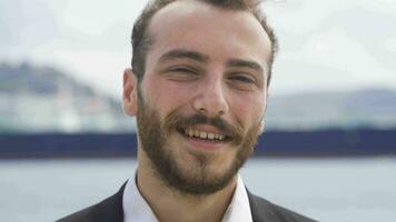 Smiling businessman looking at camera by the sea. video