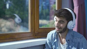 hombre mirando fuera el ventana y escuchando a música con auriculares. video